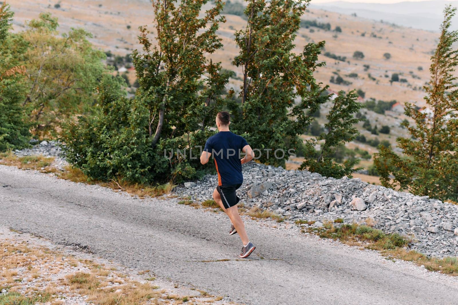 A muscular male athlete runs along a rugged mountain path at sunrise, surrounded by breathtaking rocky landscapes and natural beauty.