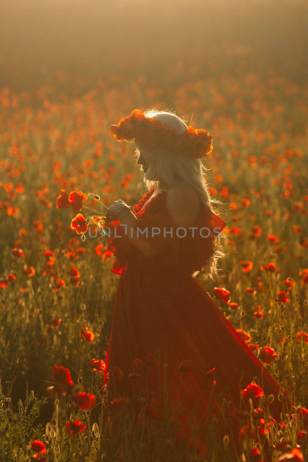 A woman in a red dress is standing in a field of red flowers. She is holding a flower in her hand and wearing a flower crown. The scene is serene and peaceful