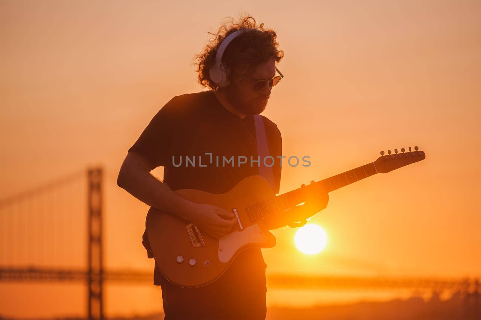 Hipster street rock musician in black playing electric guitar in street outdoors on sunset