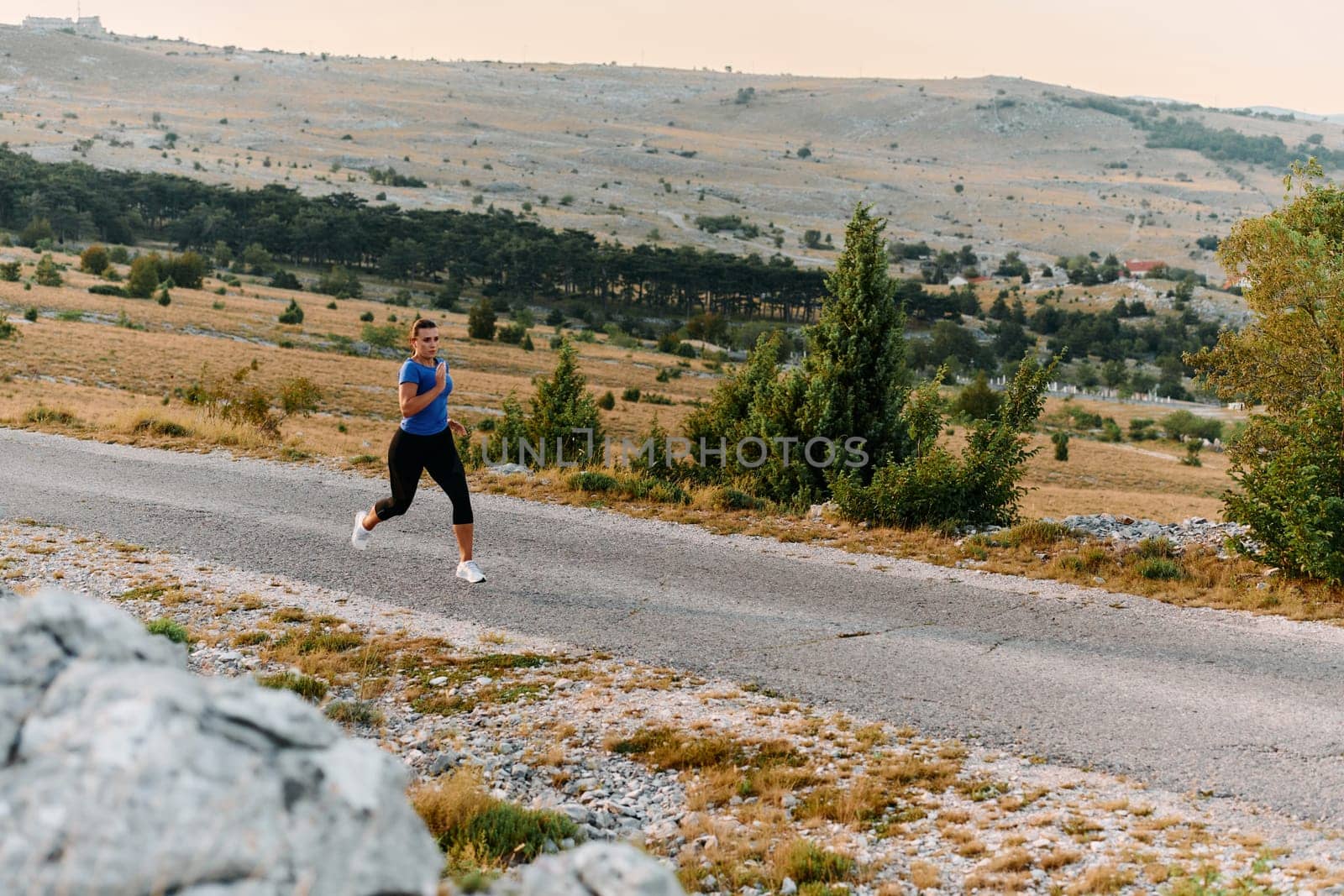 A determined female athlete runs through a forest trail at sunrise, surrounded by breathtaking natural beauty and vibrant greenery.