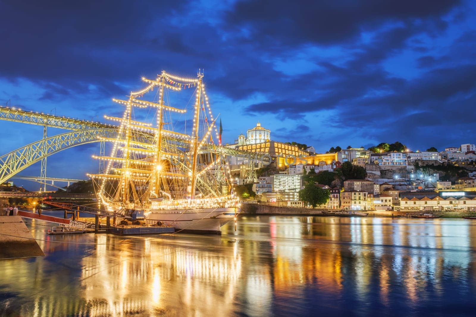 View of Vila Nova de Gaia city with a sailing ship and Dom Luis I bridge over Douro river in the evening. Porto, Portugal