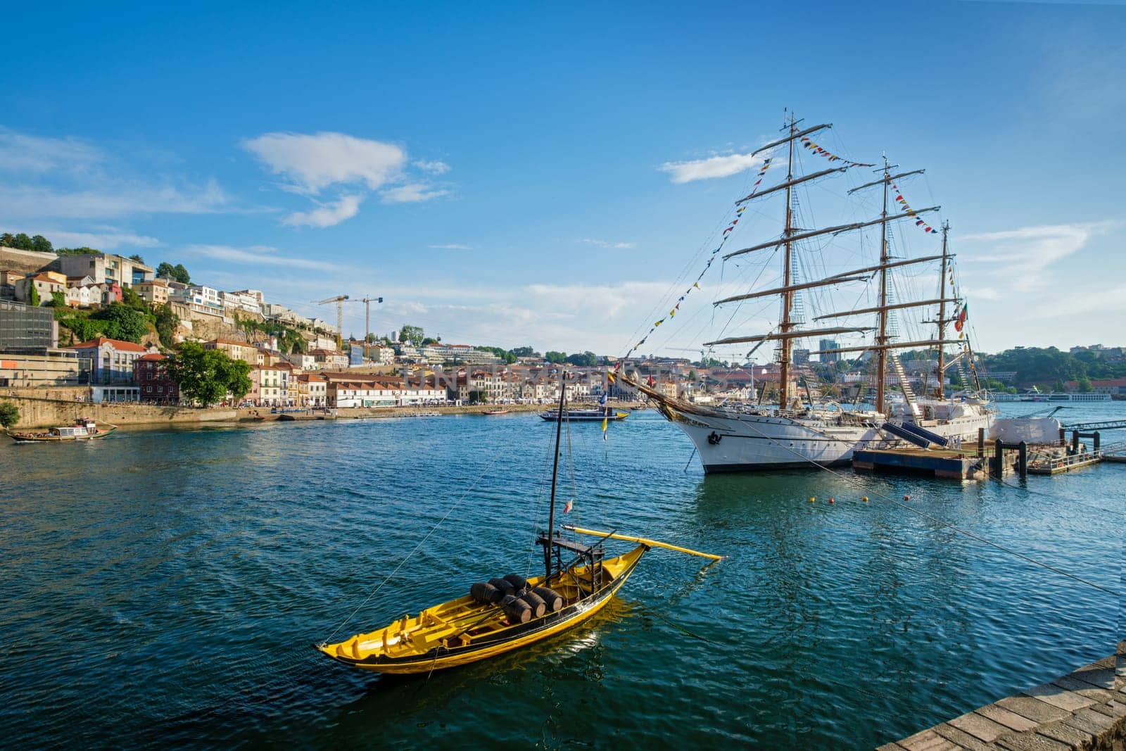 View of Vila Nova de Gaia city with sailing ship and traditional boat with port wine barrels and Douro river with tourist boats on sunset. Porto, , Portugal