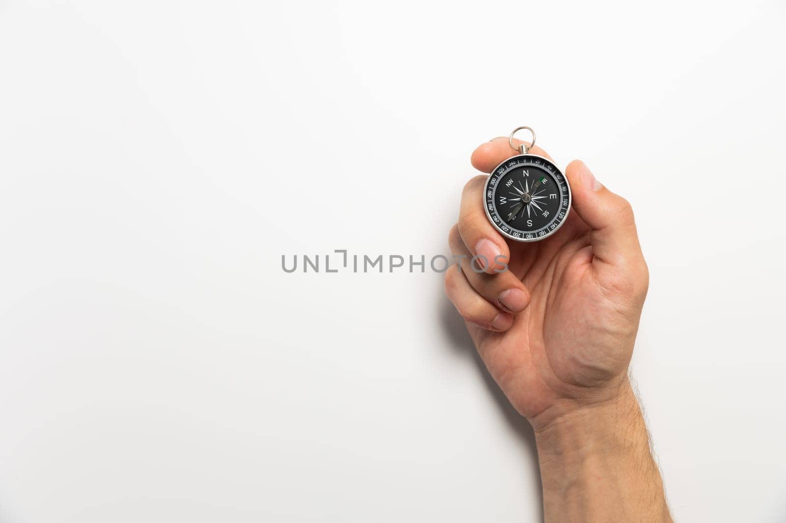 Male hand holding magnetic compass on white background with copy space.