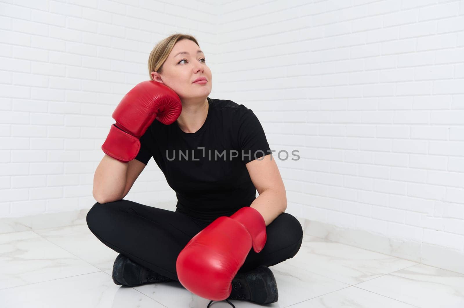 Authentic portrait of a happy European young sports woman boxer, wearing red boxing gloves, posing isolated over white wall background. Copy advertising space for text. People and sport