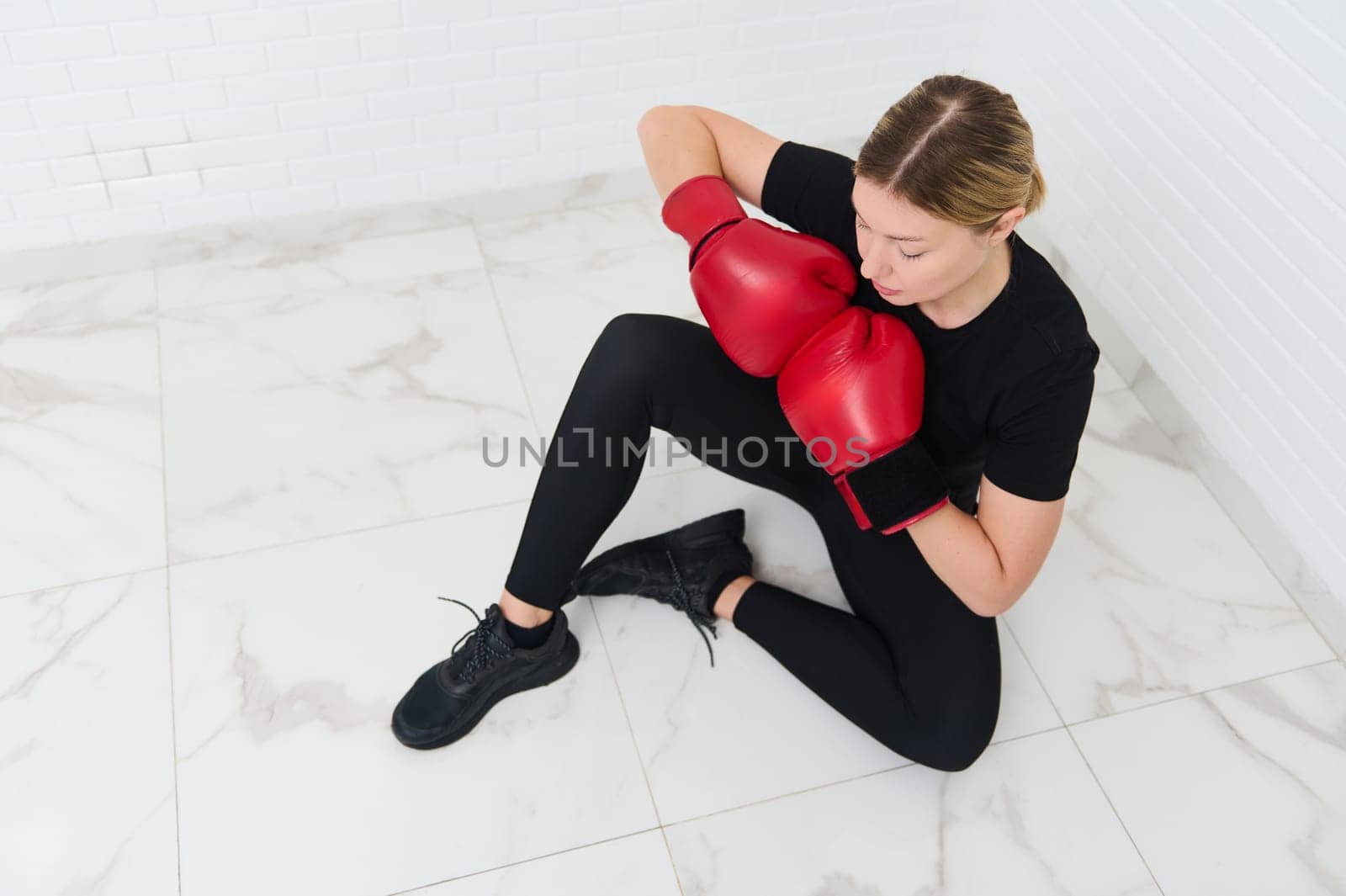 View from above of a confident young athlete woman posing in red boxing gloves, isolated over white background. Copy advertising space
