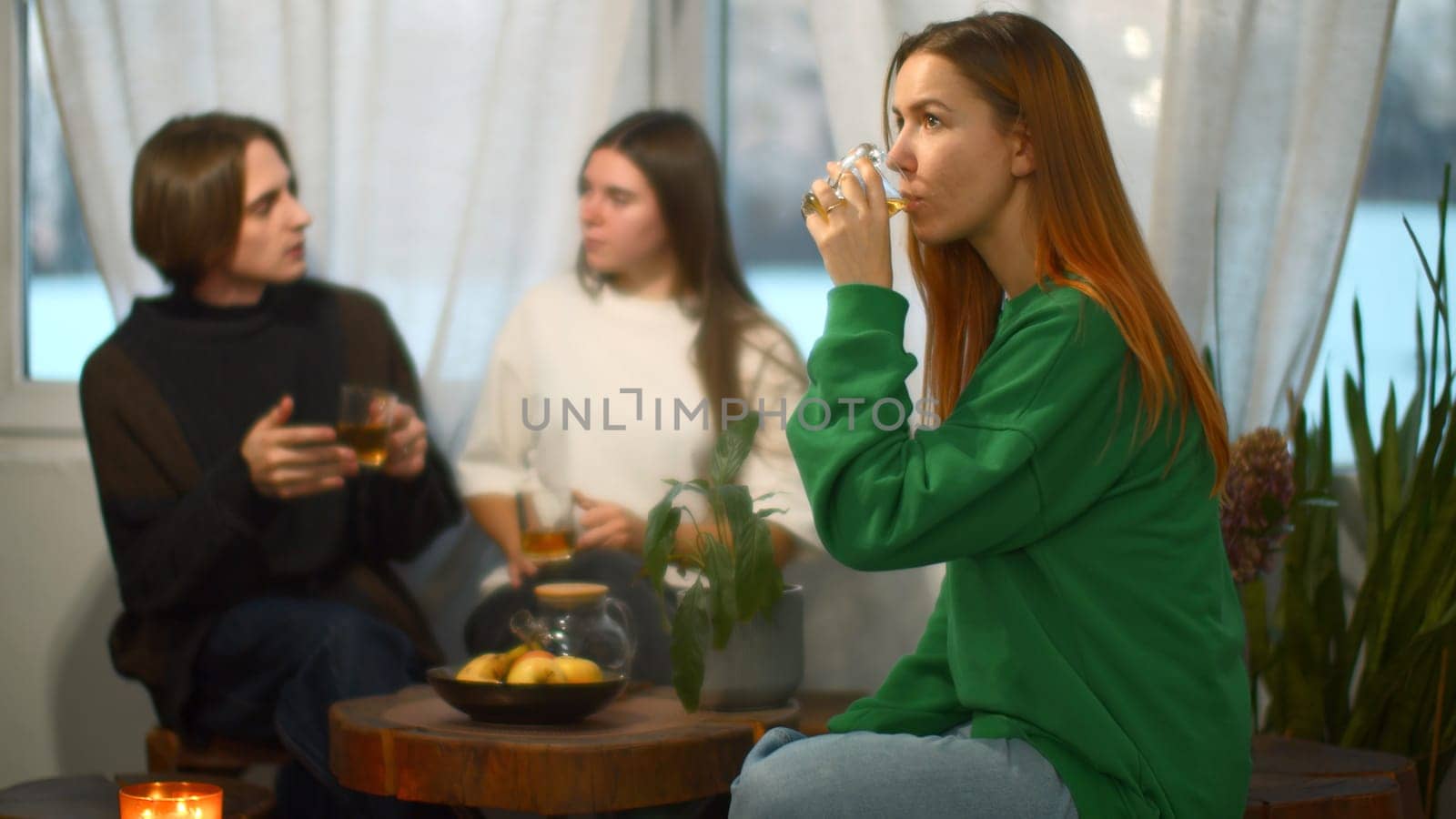 Students talk and relax in cozy cafe. Media. Beautiful young woman is drinking tea on background of talking couple. Students relax and drink tea in college cafe.