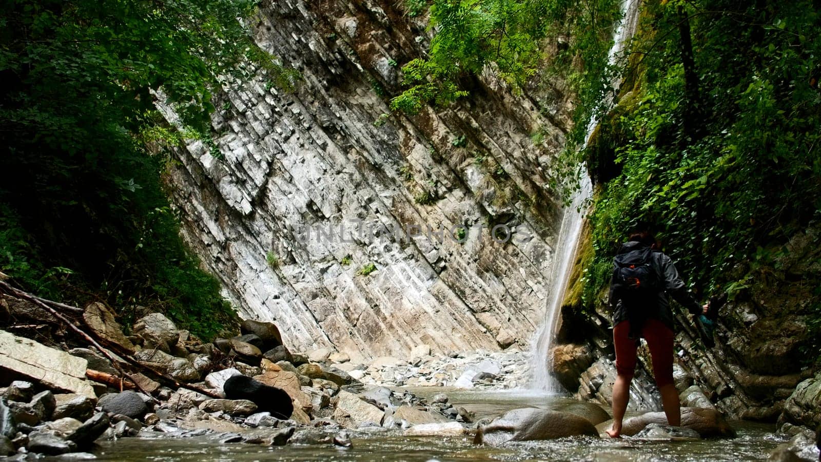 Woman crossing mountain cold water stream with stones. Creative. Hiker in picturesque place