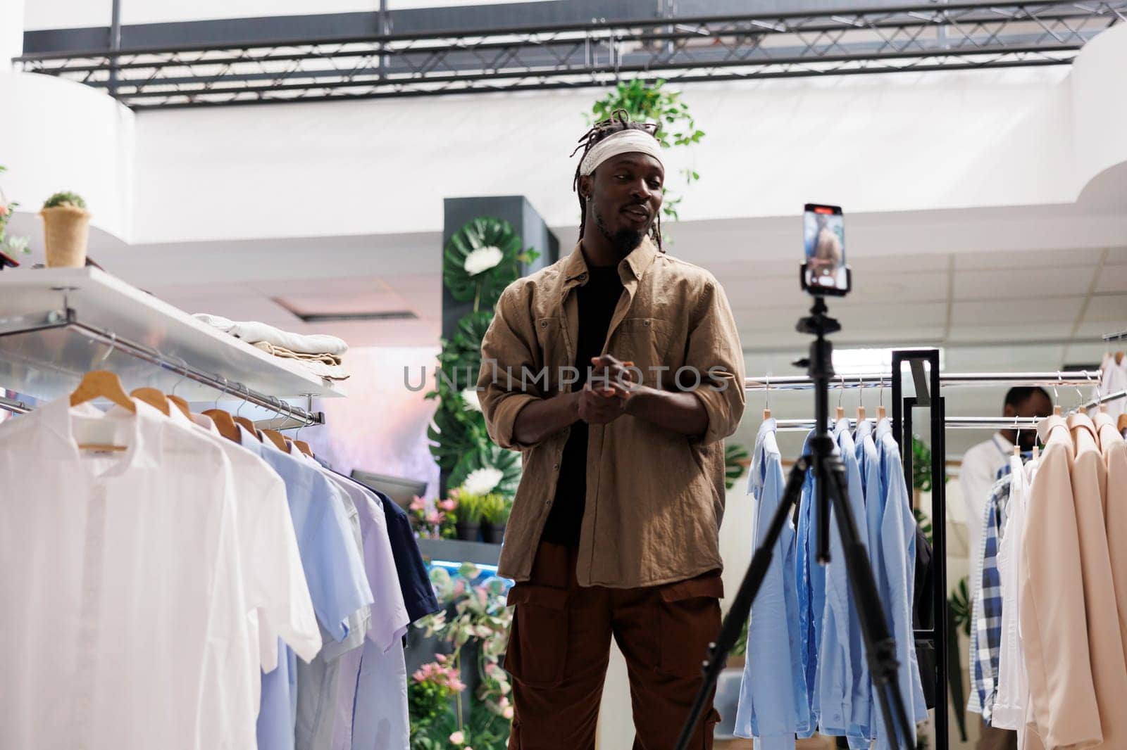 African american blogger recording promotional video in clothing store to attract customers. Stylist talking about new fashion collection on smartphone camera and advertising brand in shop