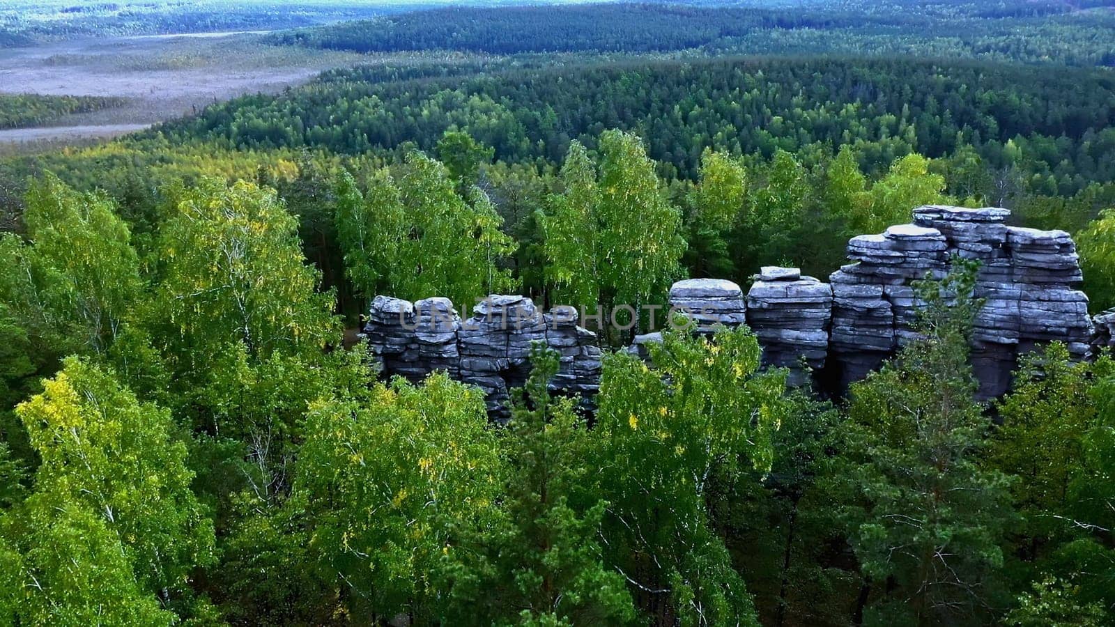 Aerial view of rock cliffs among green summer trees. Footage. Tops of the mountain cliffs in green forest