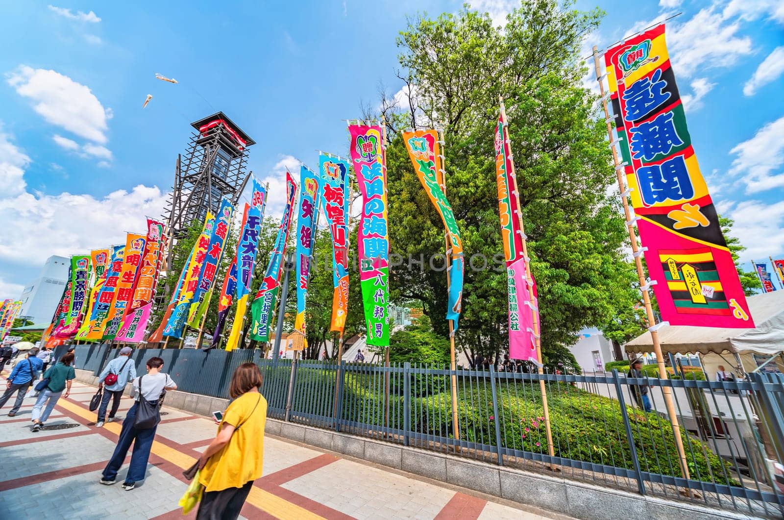 tokyo, ryogoku - may 17 2024: Japanese spectators walking along vibrant Japanese sumo nobori flags lining the path leading to the historic yagura-daiko tower of the Ryōgoku Kokugikan Sumo Stadium.