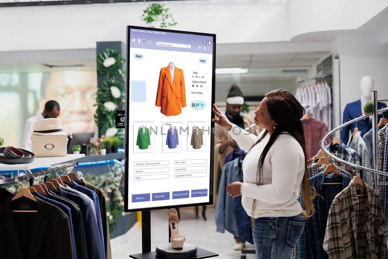 African american client selecting items to buy from self service checkout kiosk, reviewing modern clothes and sizes on interactive monitor. Young woman looking at products on board.