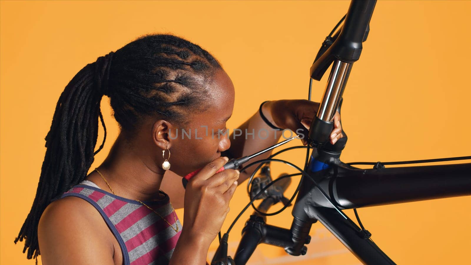 BIPOC technician uses screwdriver to unmount bicycle handlebars, testing components quality in studio background atelier shop. Specialist mechanic unscrewing bike parts in order to mend them, camera A