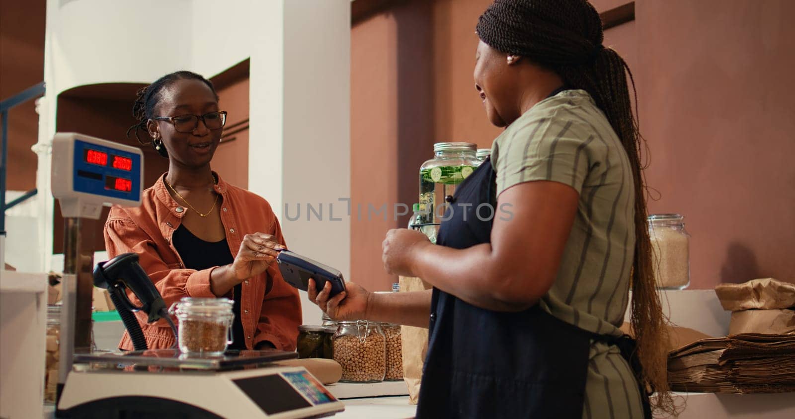 Woman using card payment at pos to buy fresh produce, choosing ripe colorful fruits and vegetables for healthy nutrition. Client paying for organic locally grown goods at checkout. Handheld shot.