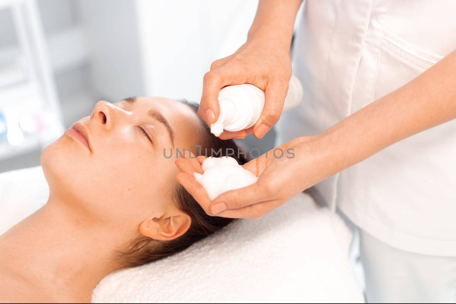Esthetician preparing to apply cleansing foam on female face beauty procedure, moisturizing face skin, facial massage. Cosmetologist cleanses the skin with foam.