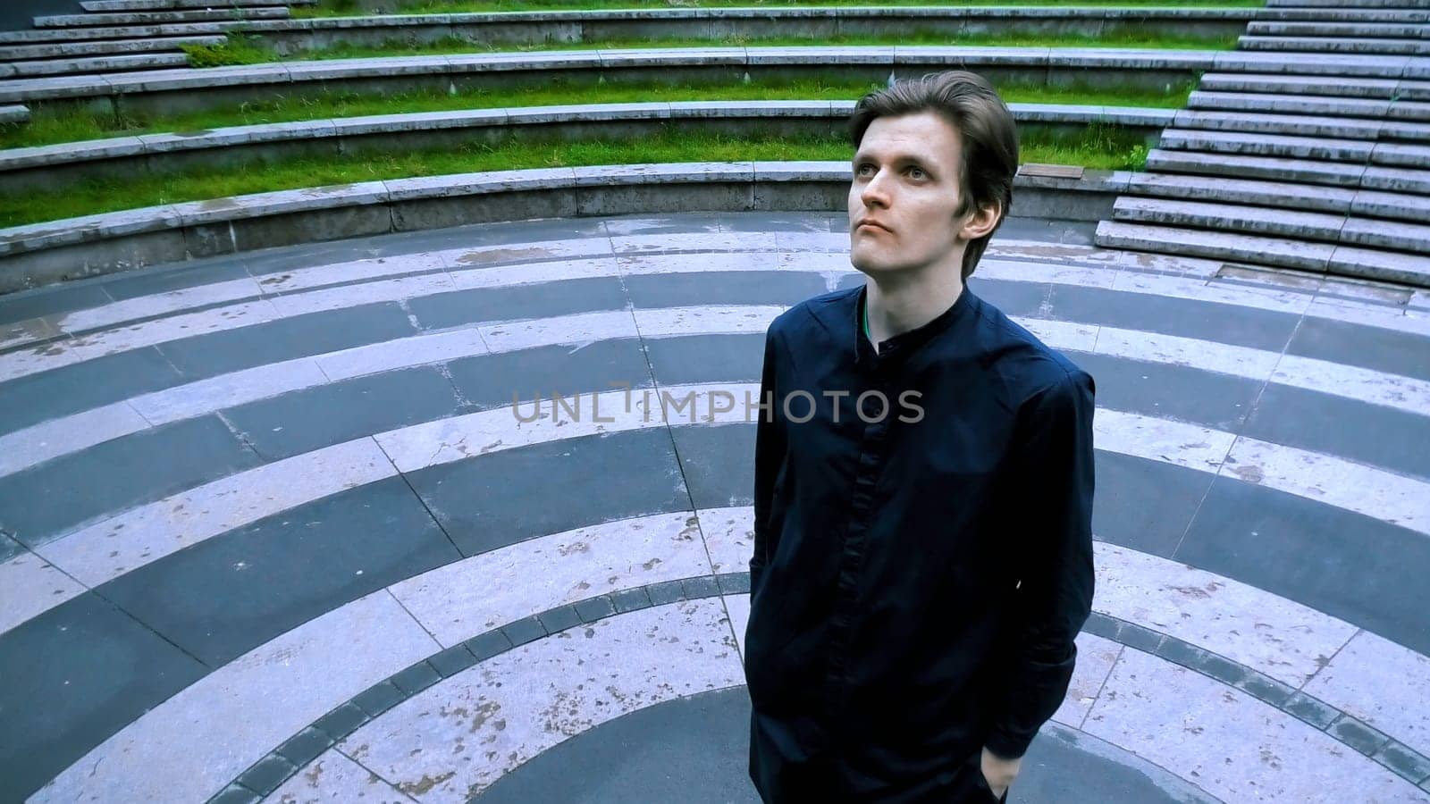 Tall man in black clothes standing in the meddle of amphitheater. Stock clip. Asphalt colored in black circles