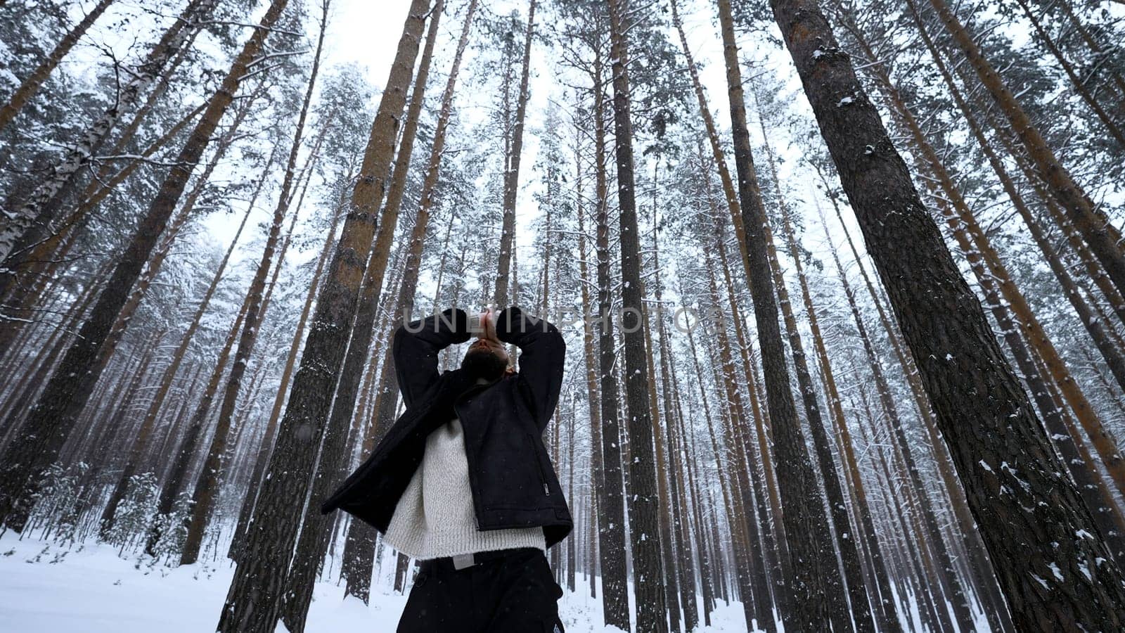 European man standing in wInter forest on a winter day. Media. Blond man raising his hands to warm up