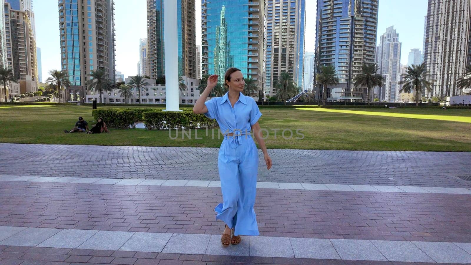 Young adult elegant beautiful woman on big city street background. Action. Lady in blue suit walking in city park