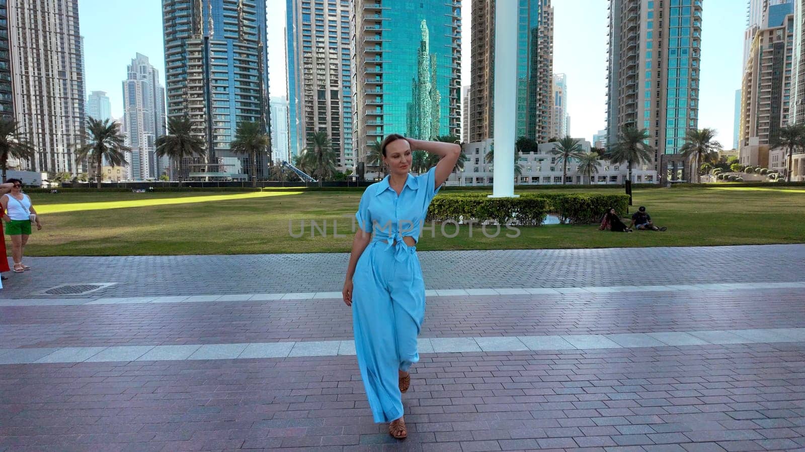 Young adult elegant beautiful woman on big city street background. Action. Lady in blue suit walking in city park