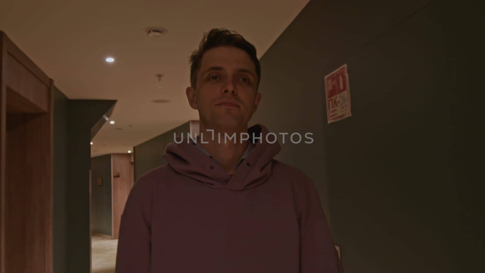 Young man in pink oversize hoodie at the hotel. Stock clip. Man walking along room doors in long corridor