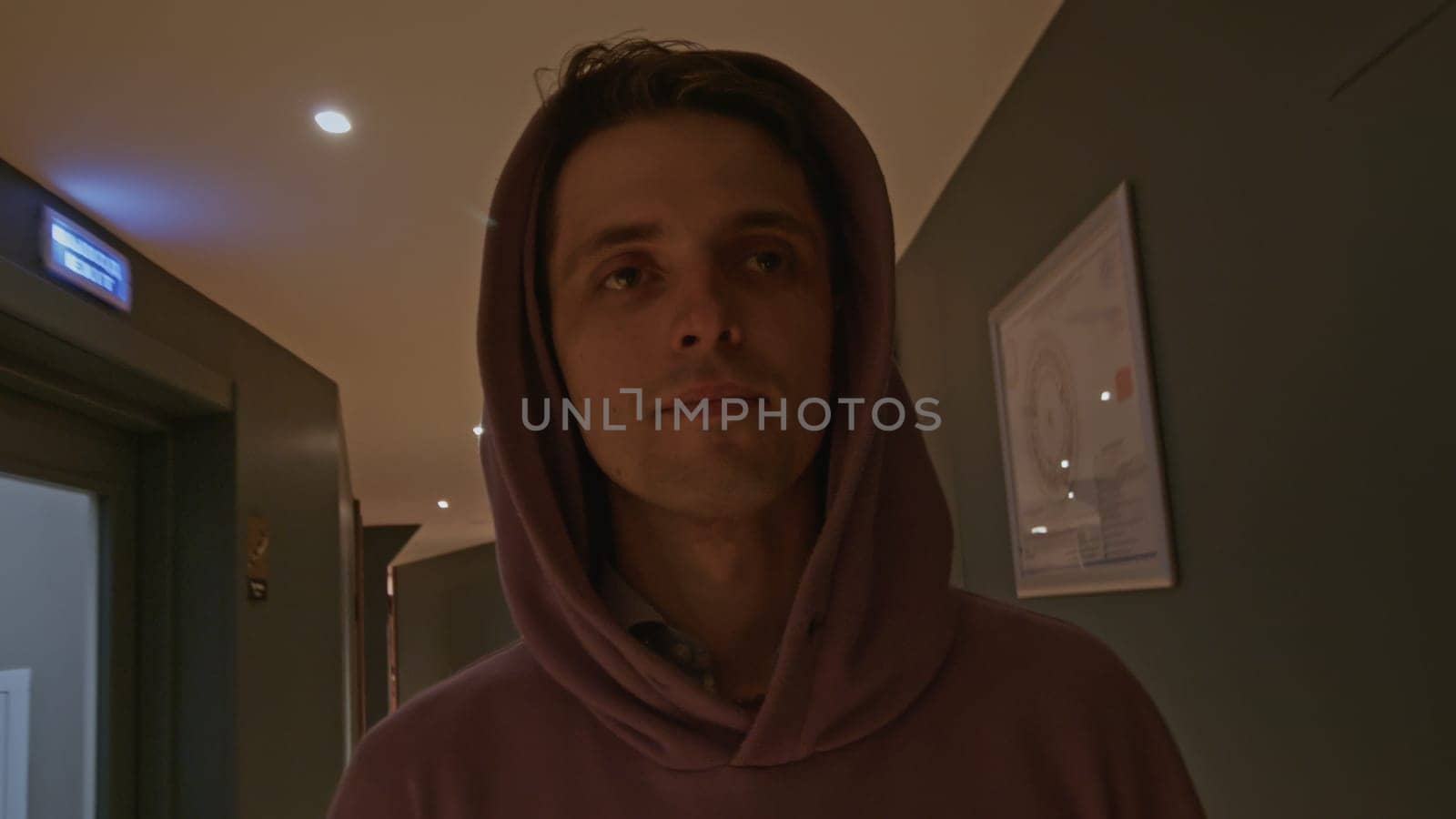 Young man in pink oversize hoodie at the hotel. Stock clip. Man walking along room doors in long corridor