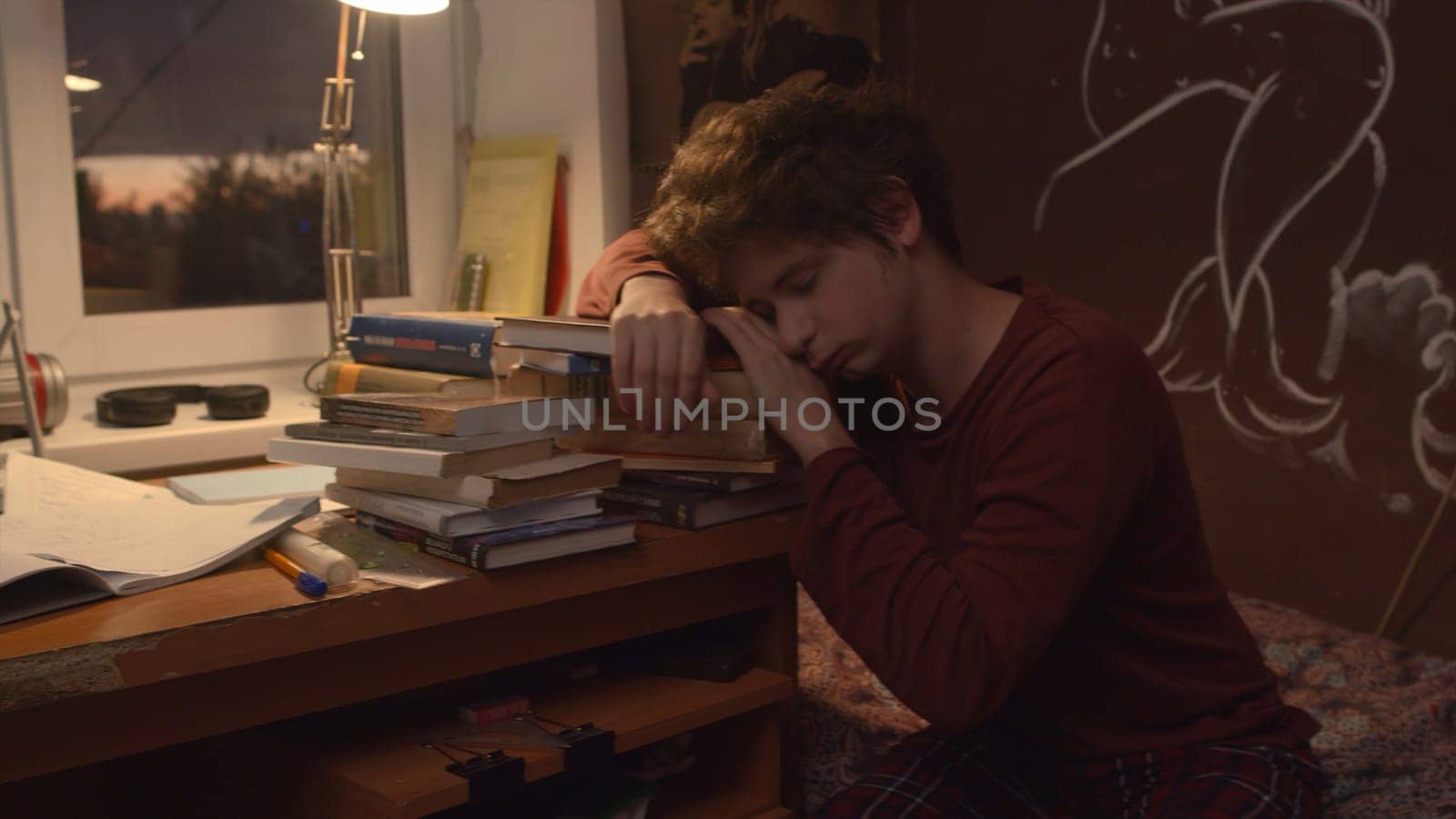 Tired student falls asleep on stack of books. Stock footage. Tired young man prepares for exam and falls asleep. Student prepares for exam and falls asleep on books at night.