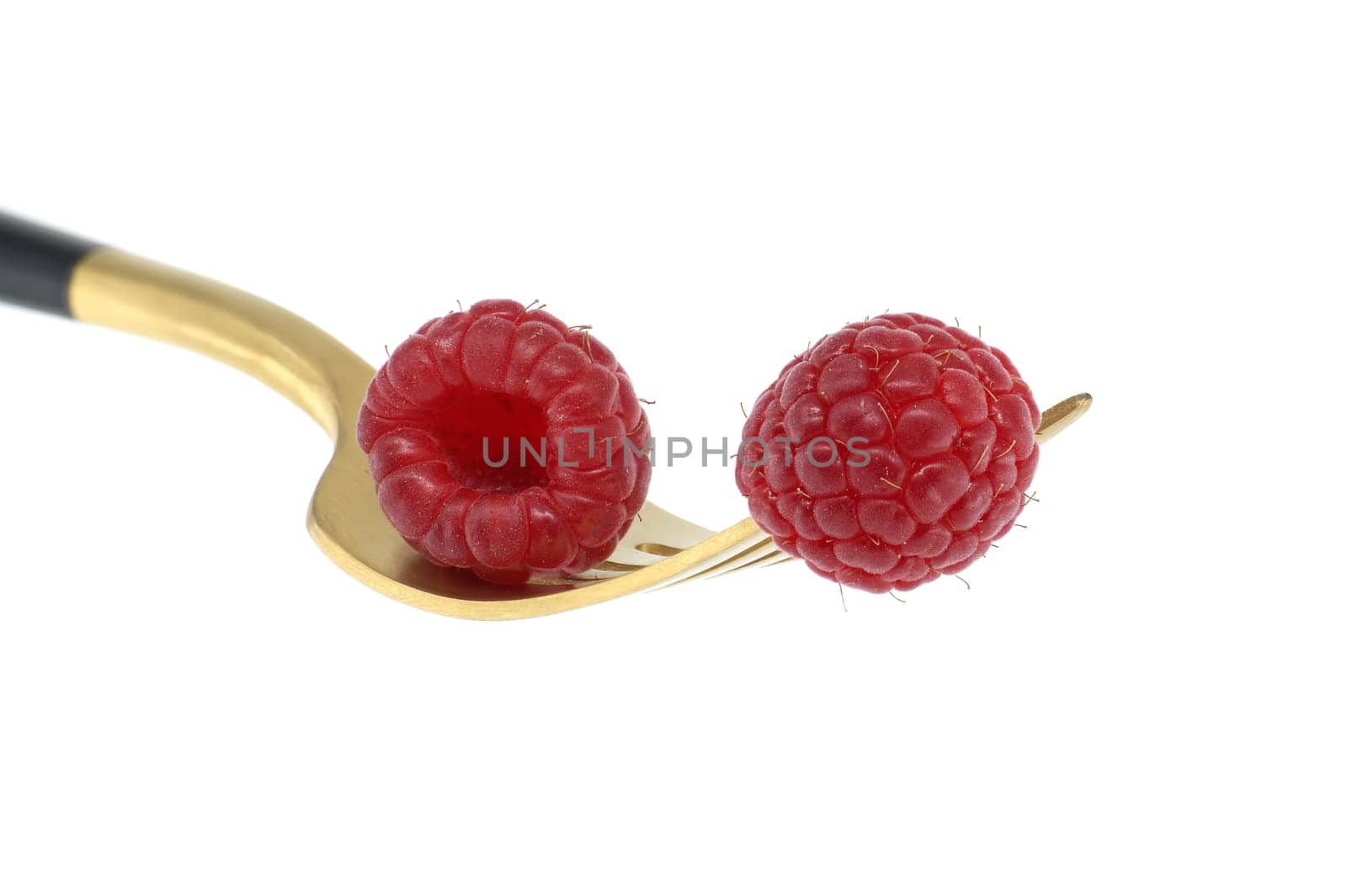 Red raspberries arranged on gold fork with a black handle, set against a white background, symbolizing a concept of healthy diet and organic food