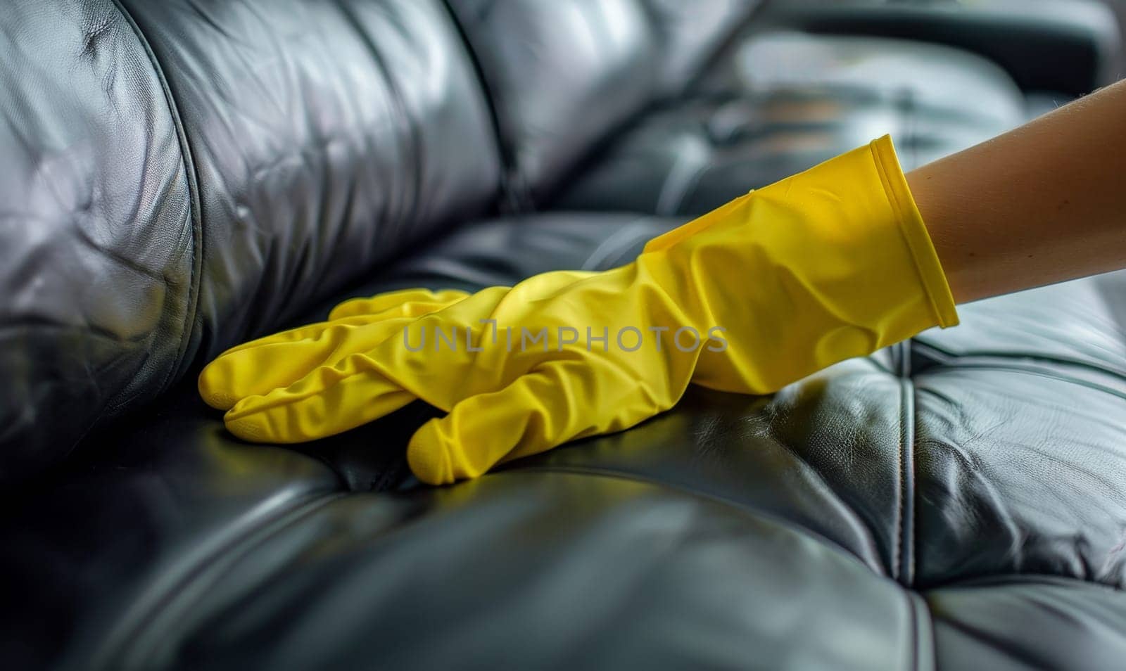 woman hand in yellow glove cleaning black leather sofa..