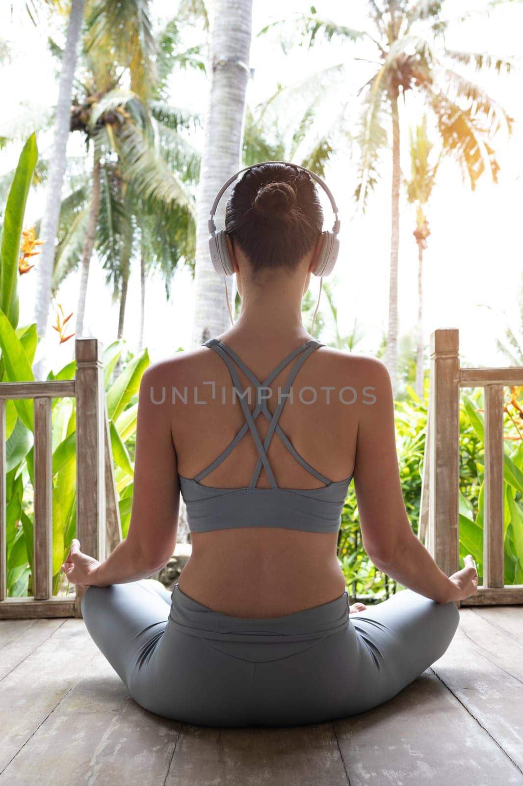 Rear view image of young woman meditating in nature using headphones. Vertical image. Healthy lifestyle and technology concept.