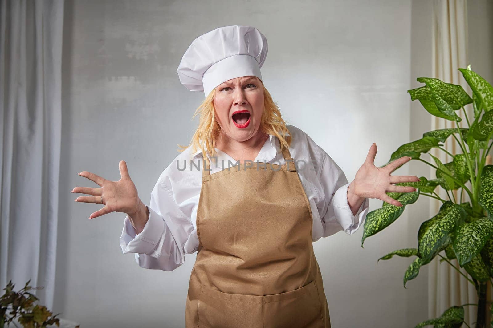 A fat funny female cook in a hat and apron poses in the kitchen and takes selfie. Good cooking and body positive