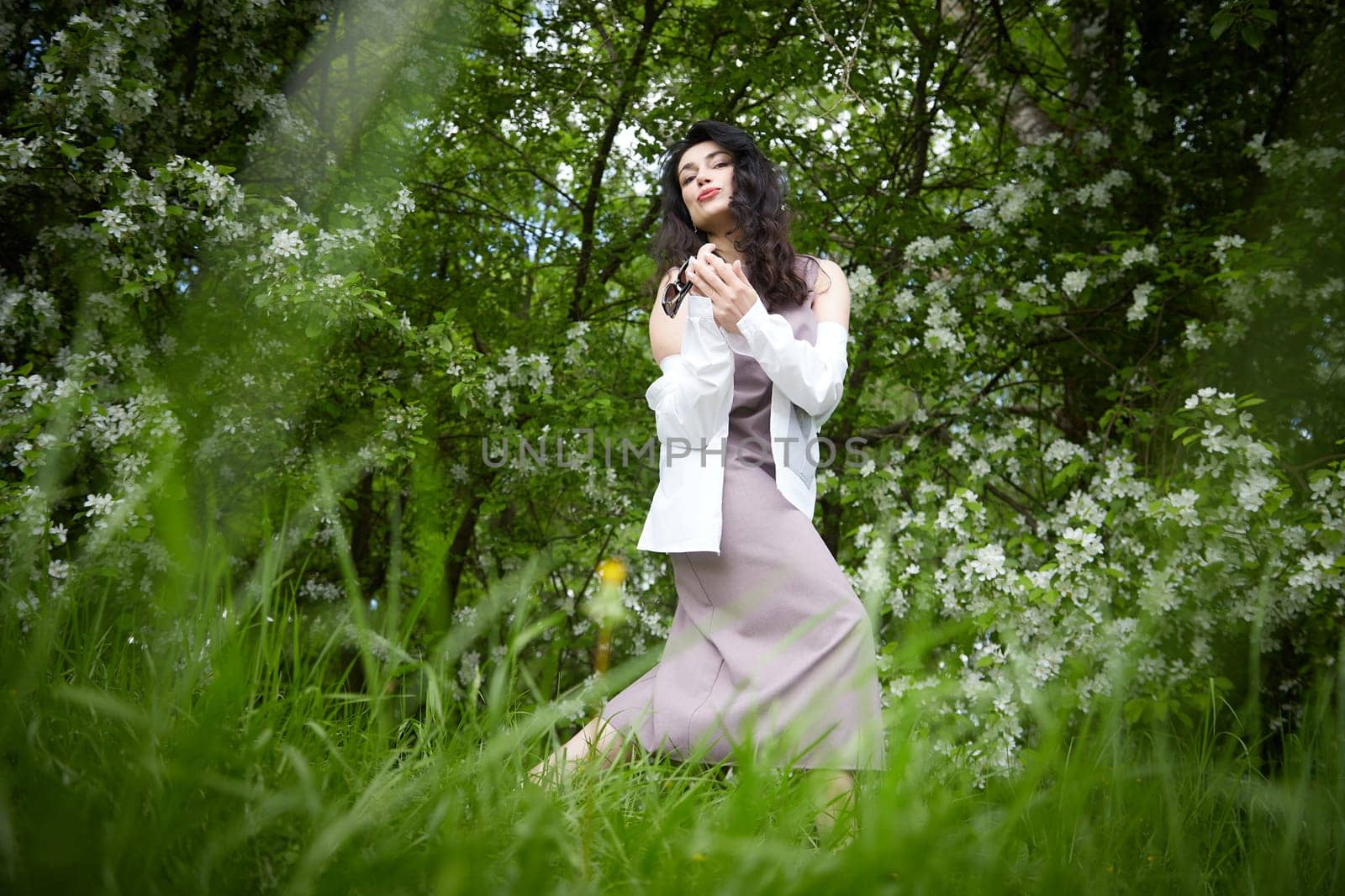 Joyous brunette woman near Blossoms of apple tree in a Spring Garden outdoors. The Concept of face and body care. The scent of perfume and tenderness