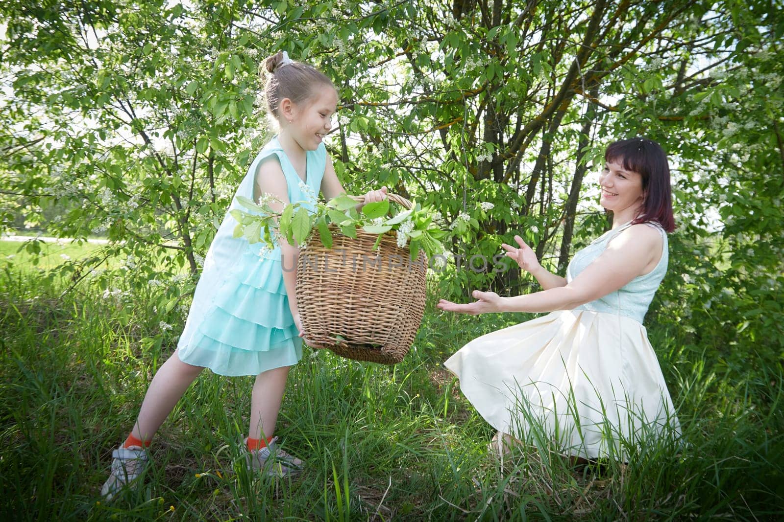 Happy mother and daughter enjoying rest, playing and fun on nature on a green lawn and with a blooming apple tree in the background. Woman and girl resting outdoors in summer and spring day by keleny