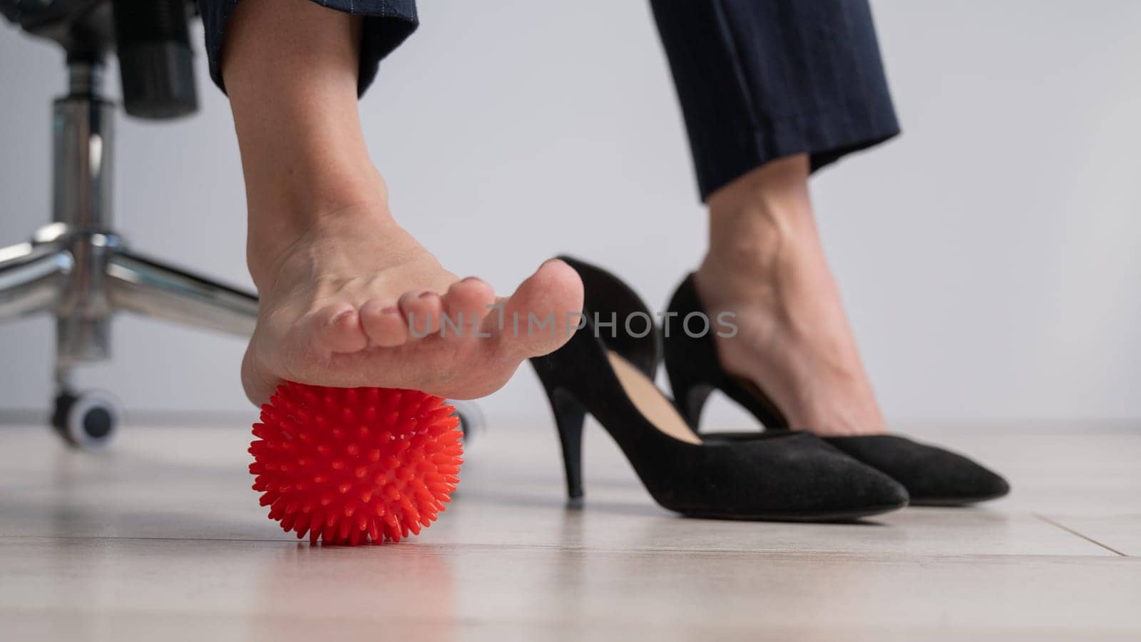 Business woman massages her feet on a massage ball with spikes