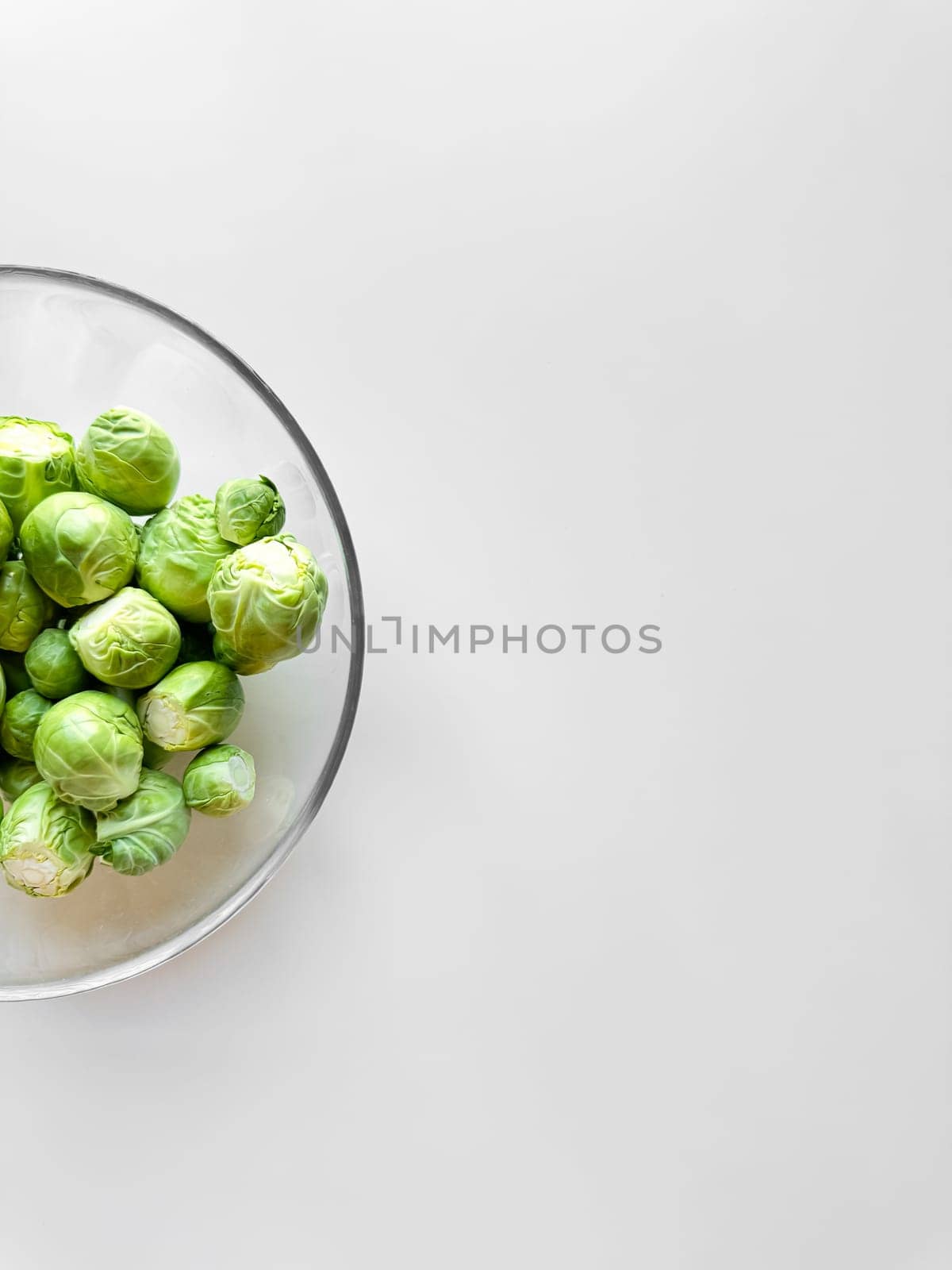 Fresh Brussels sprouts in a glass bowl on a white surface with copy space, healthy eating concept. High quality photo