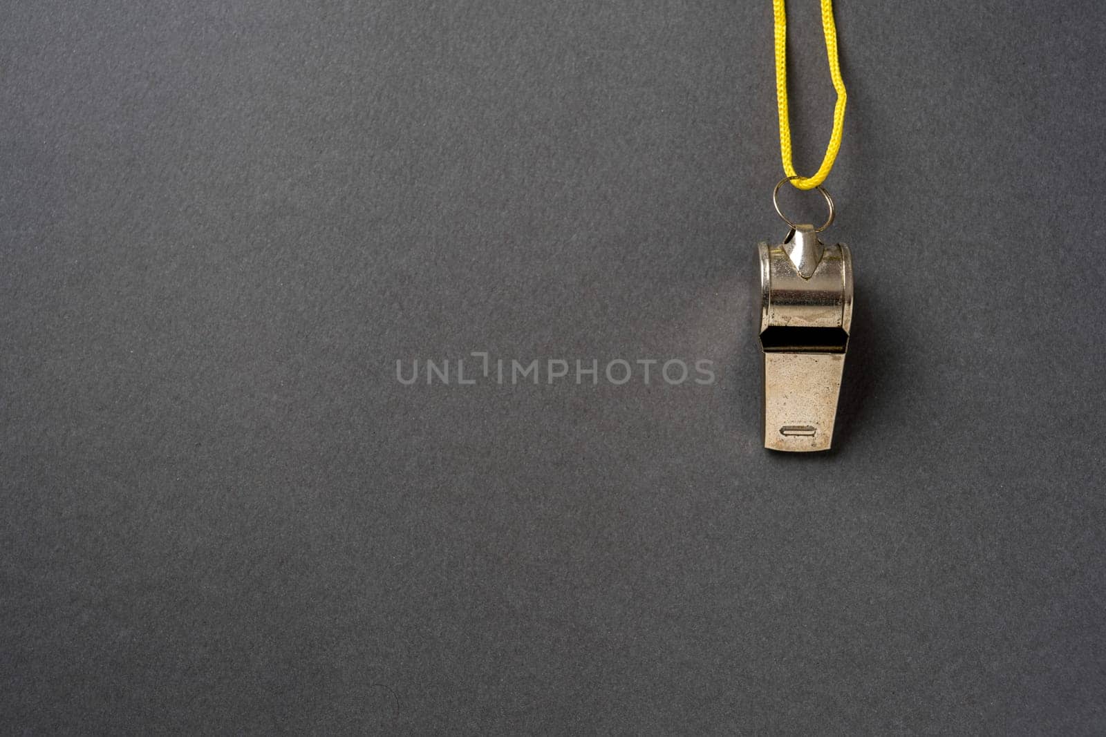 Top view of metal whistle with yellow string on dark gray background by Sonat