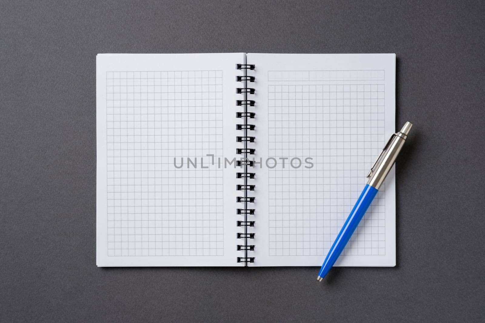 Checkered and spiral notebook on a dark gray table with a ballpoint pen next to it