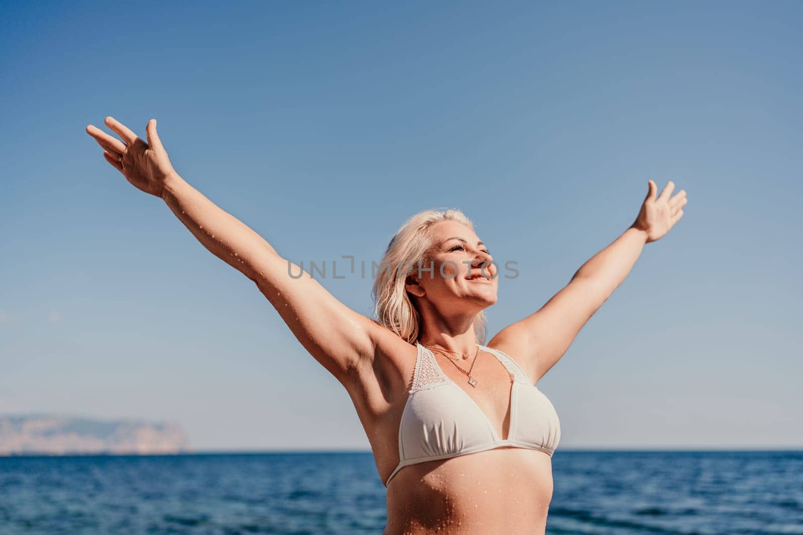 A woman is standing on the beach with her arms outstretched, smiling and enjoying the beautiful blue ocean