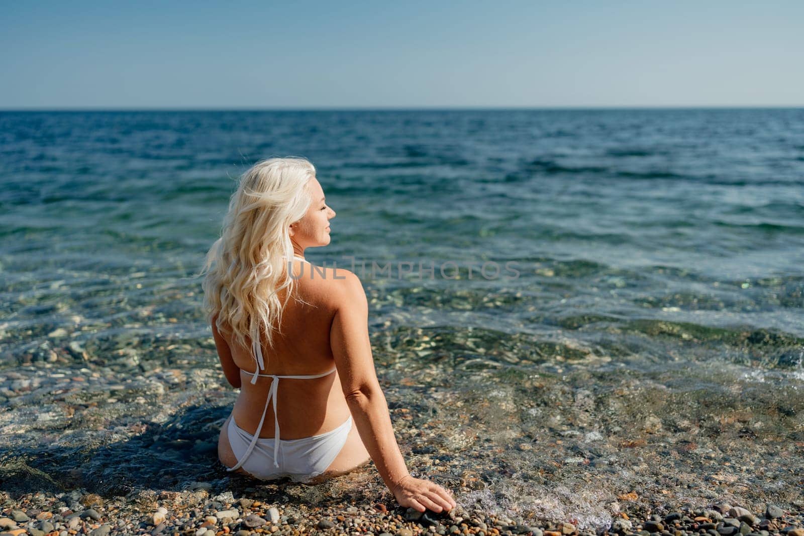 A woman in a bikini is sitting in the ocean. The water is calm and the sky is clear