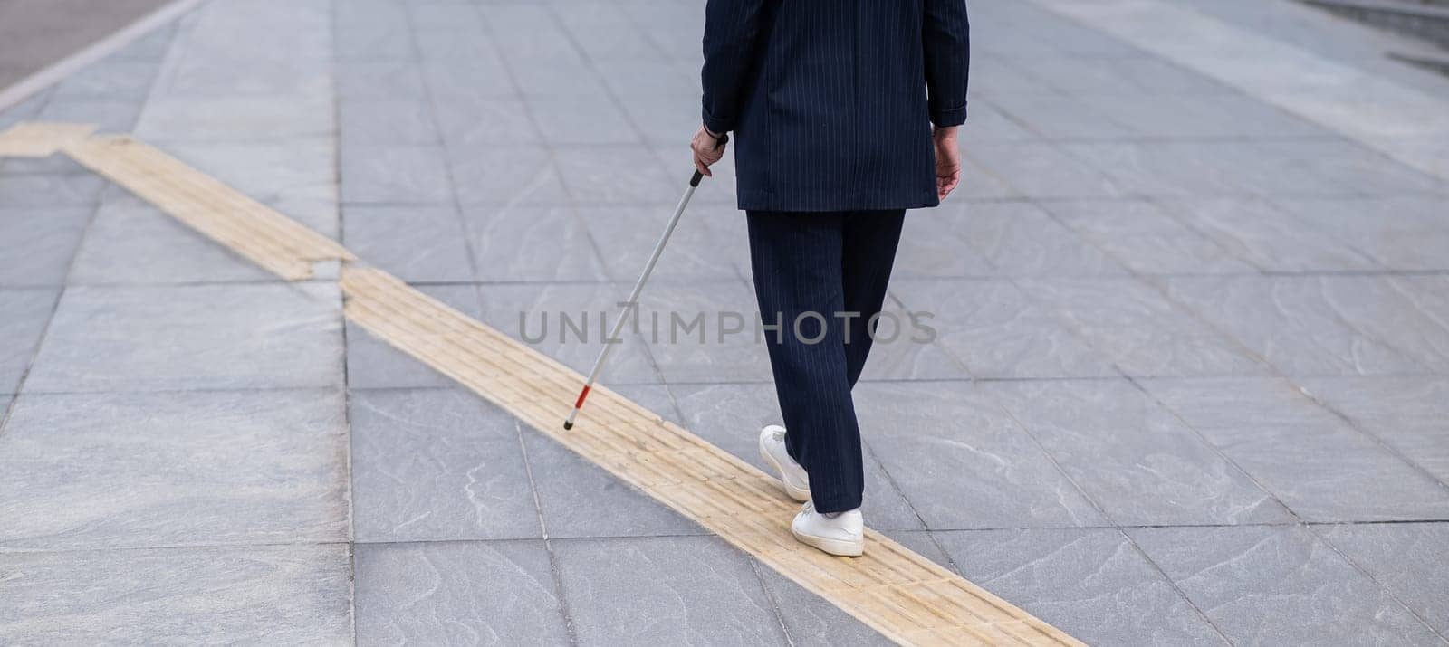 Close-up of the legs of a blind businesswoman walking along a tactile tile with a cane. by mrwed54