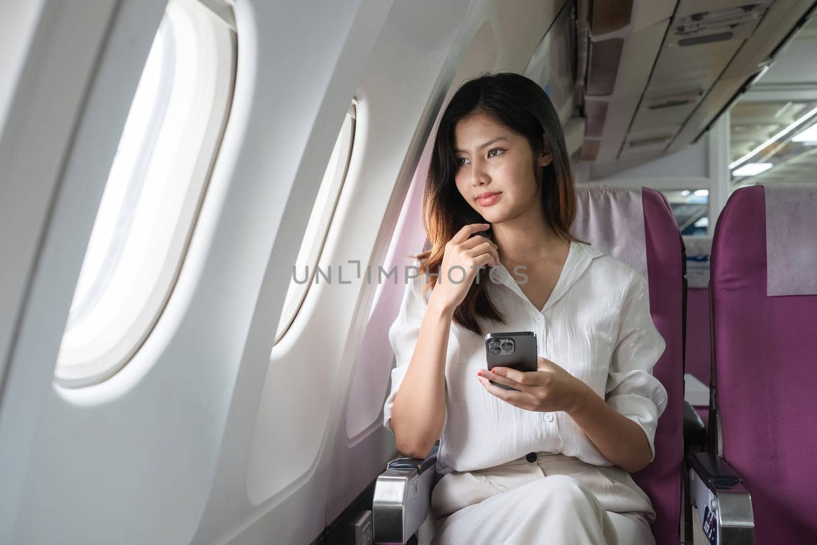 Young woman traveling on airplane and using smartphone. Concept of travel and technology.
