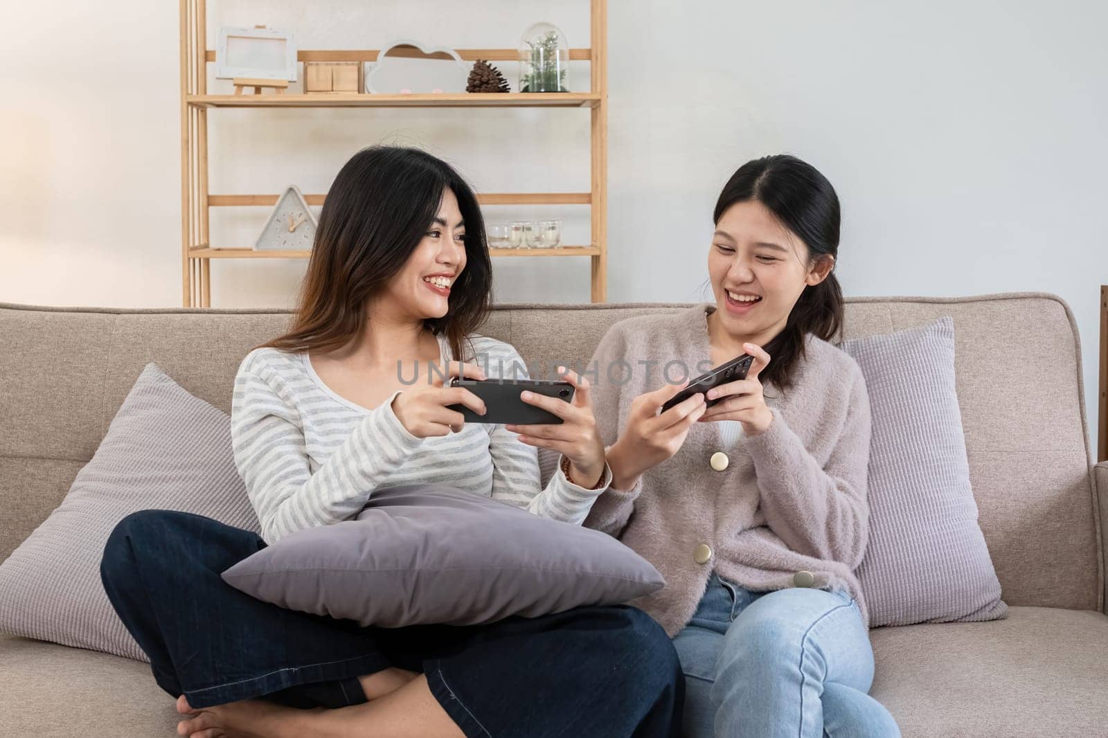 Two young women playing games on smartphones together at home. Concept of friendship and technology by wichayada