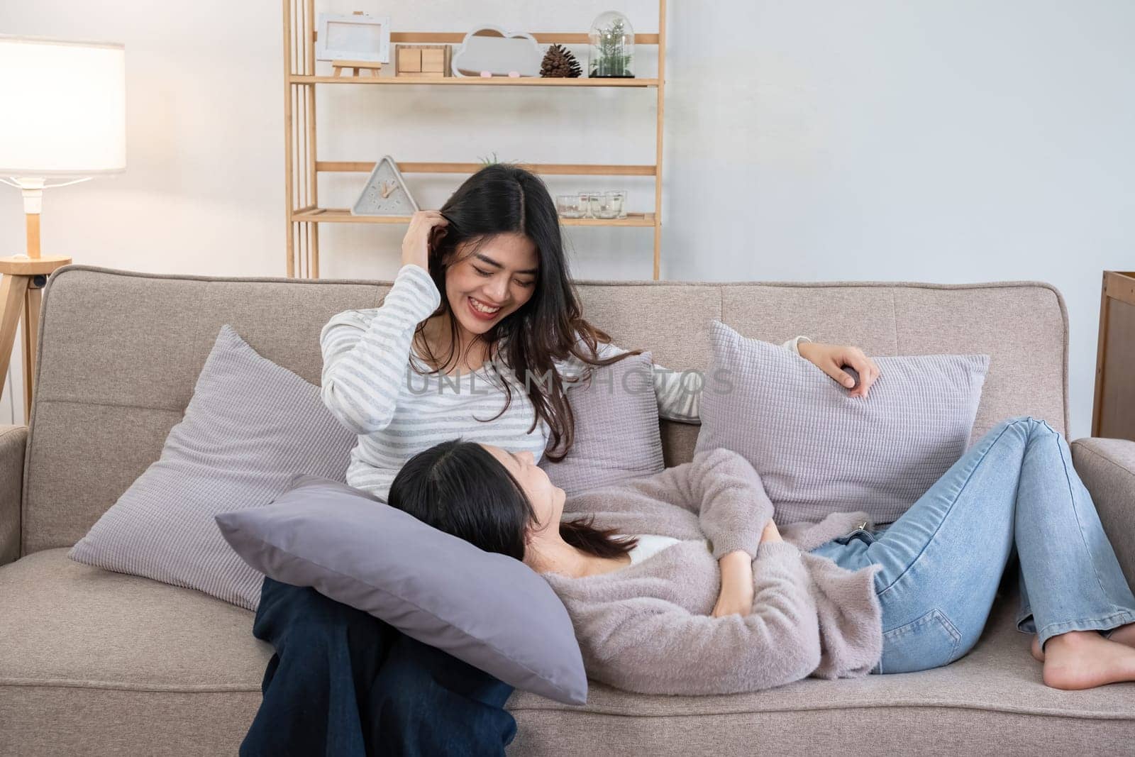 Two young women relaxing on couch at home. Concept of friendship and comfort by wichayada