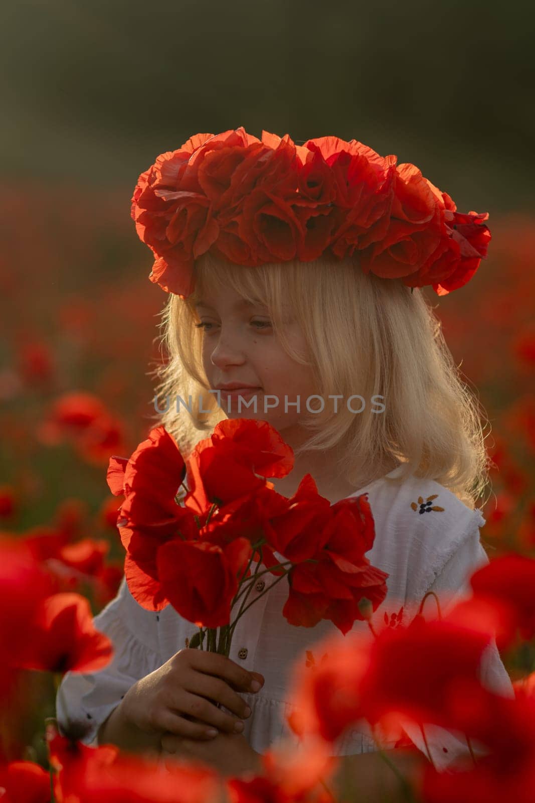 A young girl wearing a red flower crown is standing in a field of red flowers. She is holding a bouquet of red flowers in her hand. Concept of innocence and joy