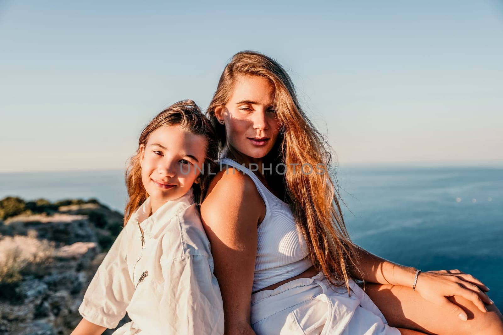 Close up portrait of mom and her teenage daughter hugging and smiling together over sunset sea view. Beautiful woman relaxing with her child.