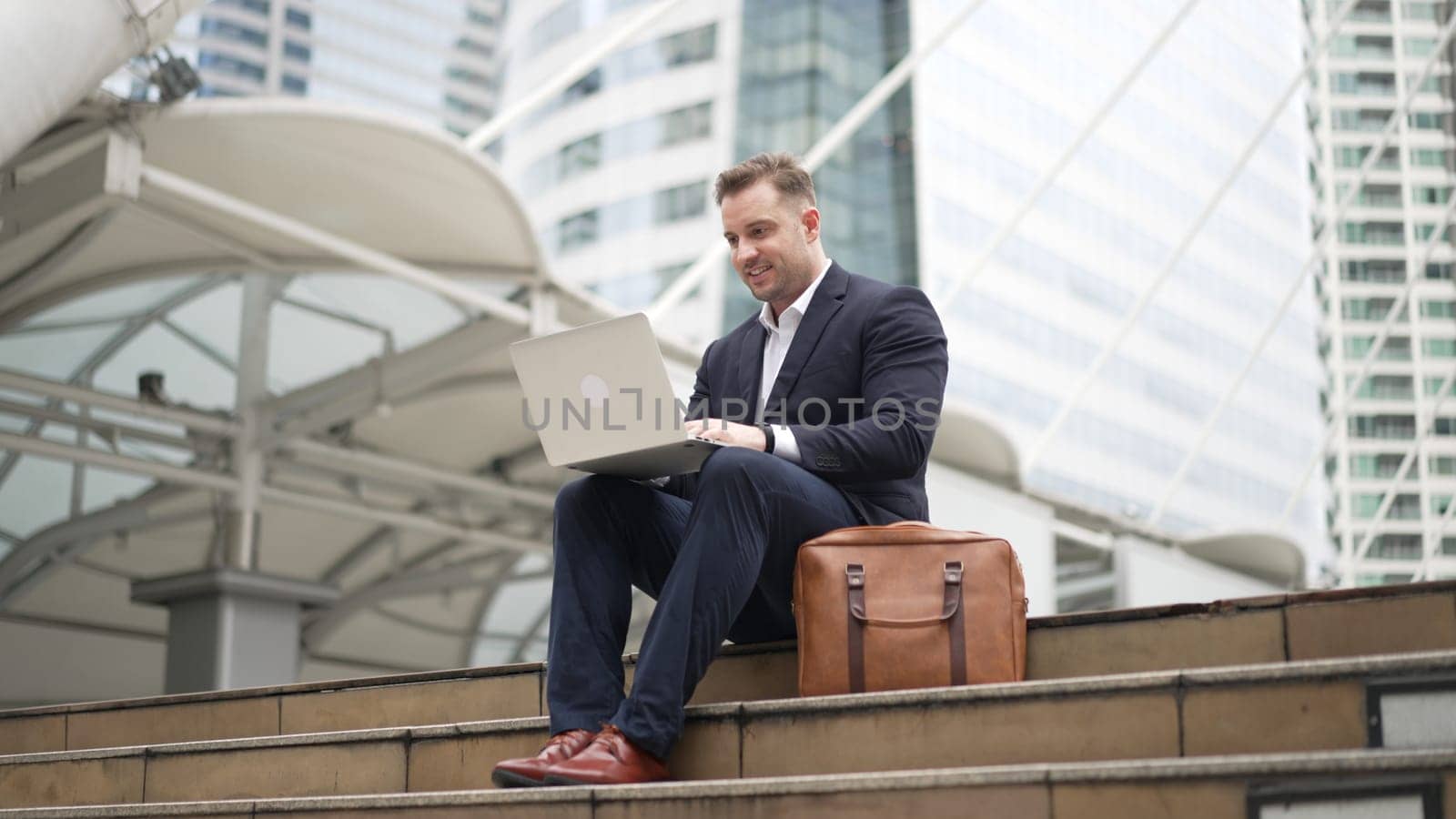 Low angle view of professional business man working on laptop at stairs. Caucasian project manager using computer to plan marketing strategy and communicate with financial team at urban city. Urbane.