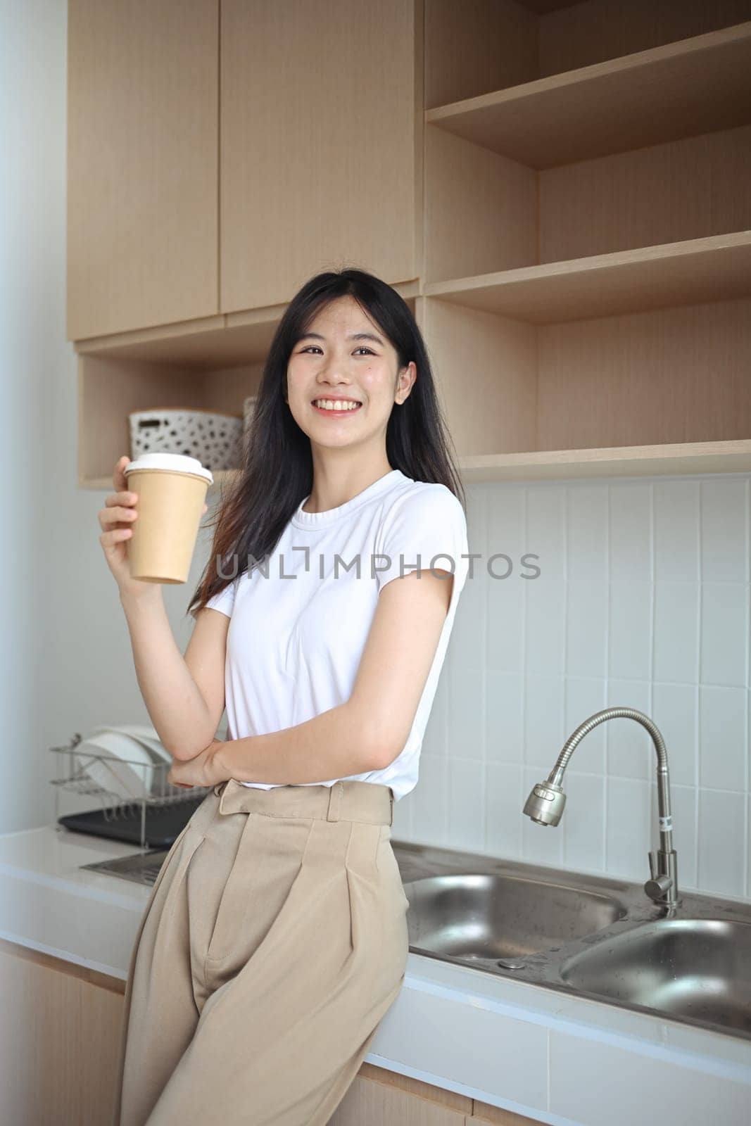 Charming young Asian woman enjoying fresh aromatic coffee standing in the kitchen.