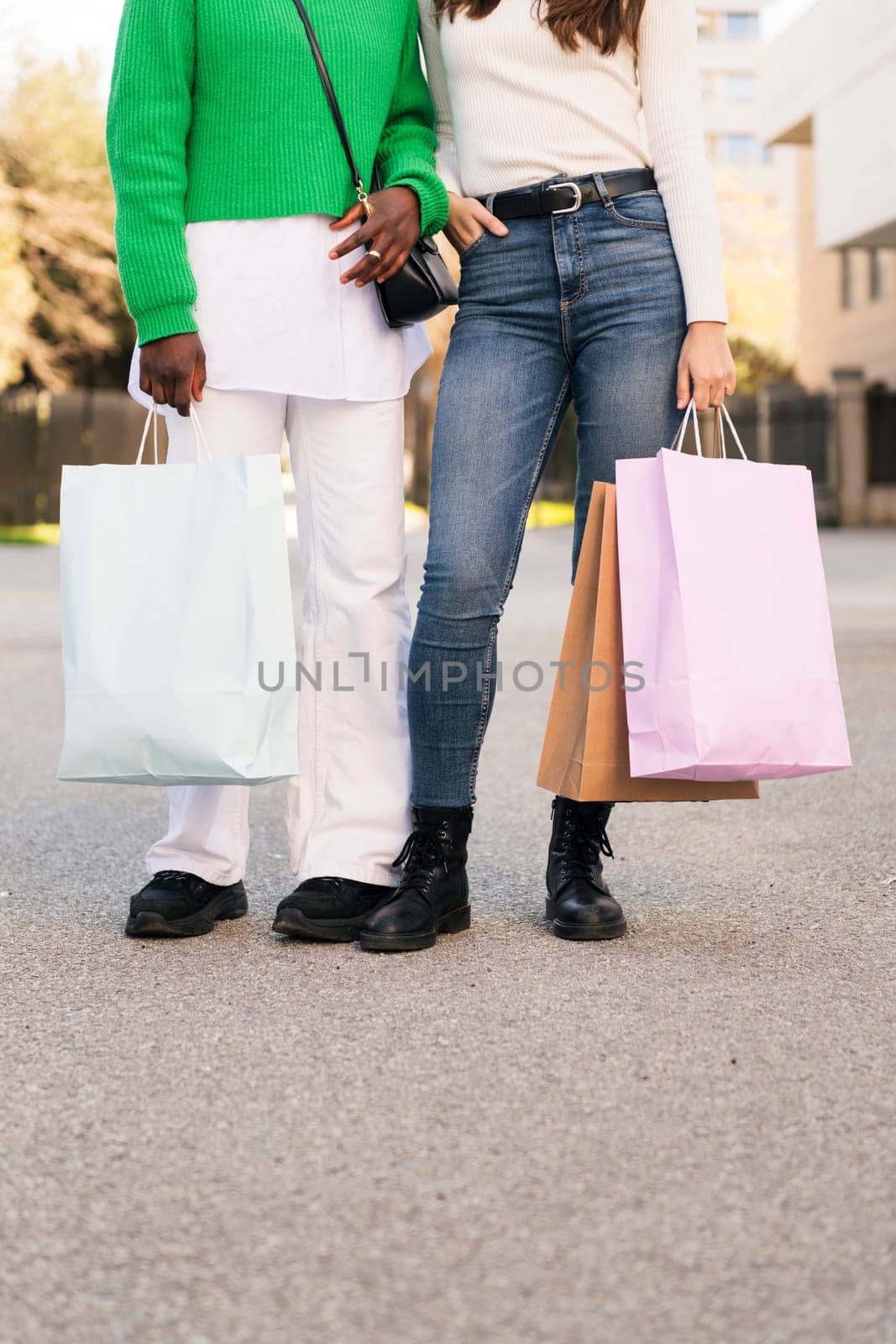 front view of the legs of two unrecognizable women standing in a city park with shopping bags, concept of friendship and urban lifestyle, copy space for text