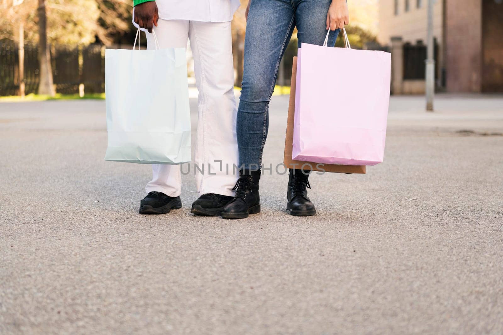 front view of the legs of two unrecognizable women standing in a city park with shopping bags, concept of friendship and urban lifestyle, copy space for text