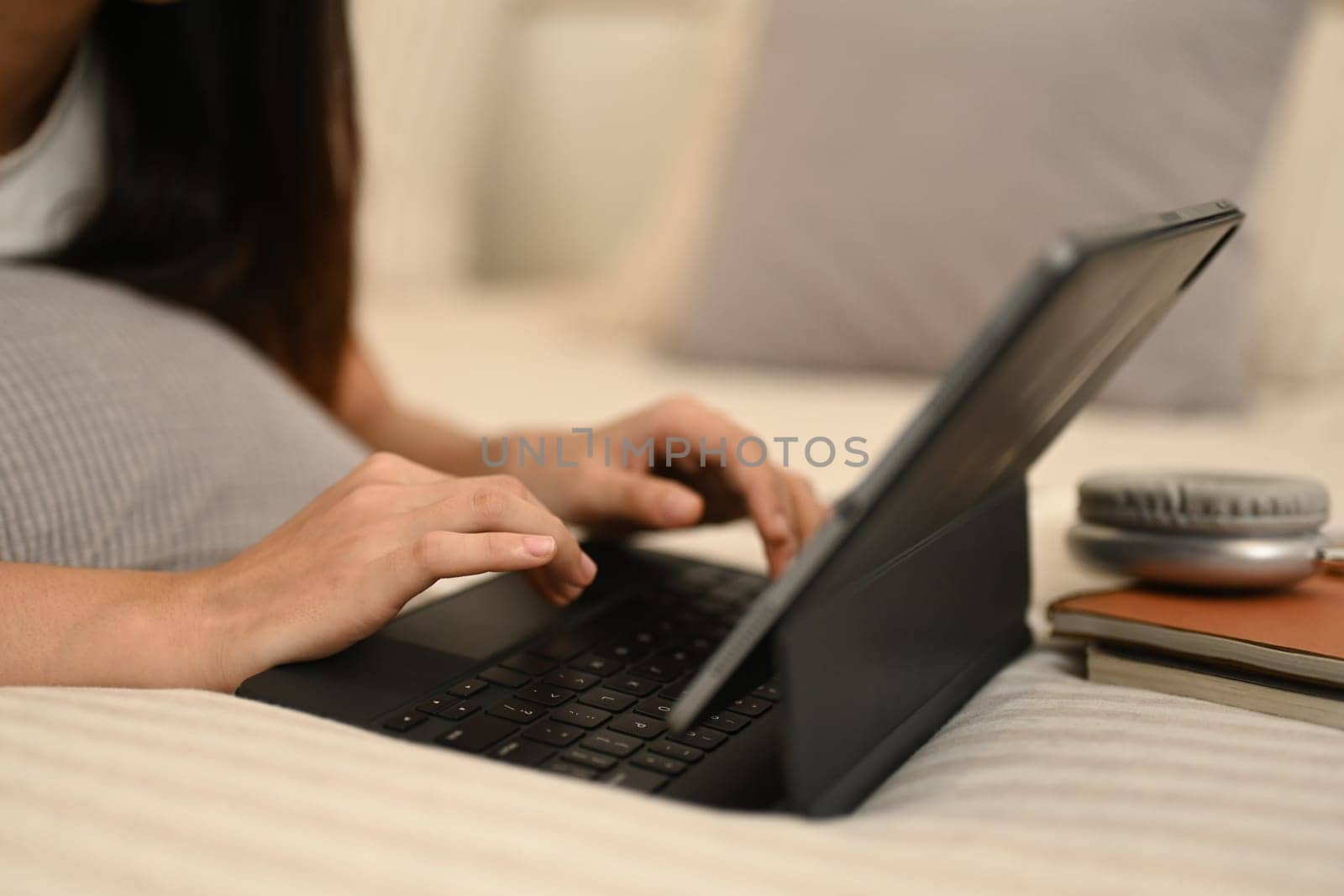 Cropped shot relaxed young woman lying on bed at home, using digital tablet.