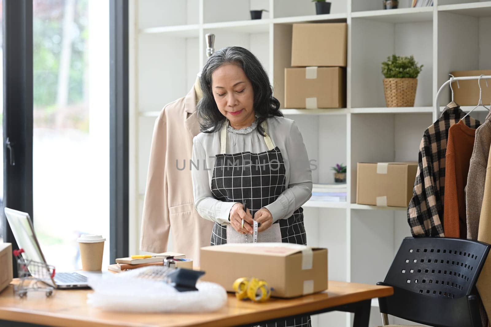 Senior woman small business owner packing parcel boxes of product for shipping to customers.