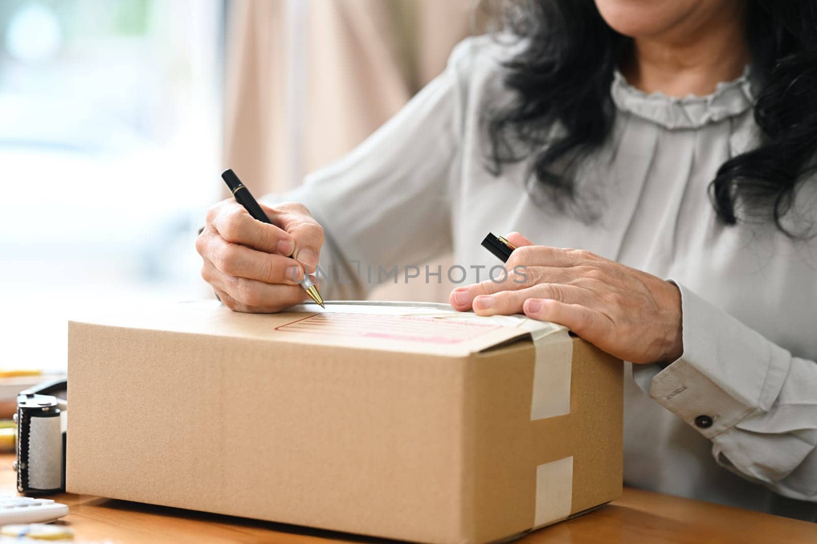 Close up senior female entrepreneur writing address on cardboard for delivery to customers.